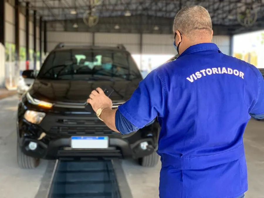 Vistoriador uniformizado avaliando um veículo na linha de inspeção
