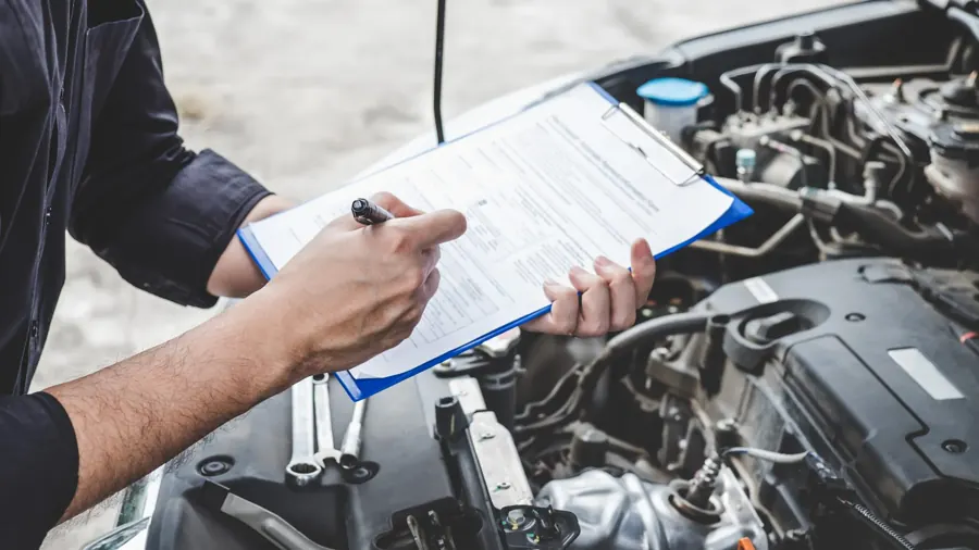 Profissional conferindo documentação ao lado do motor de um veículo